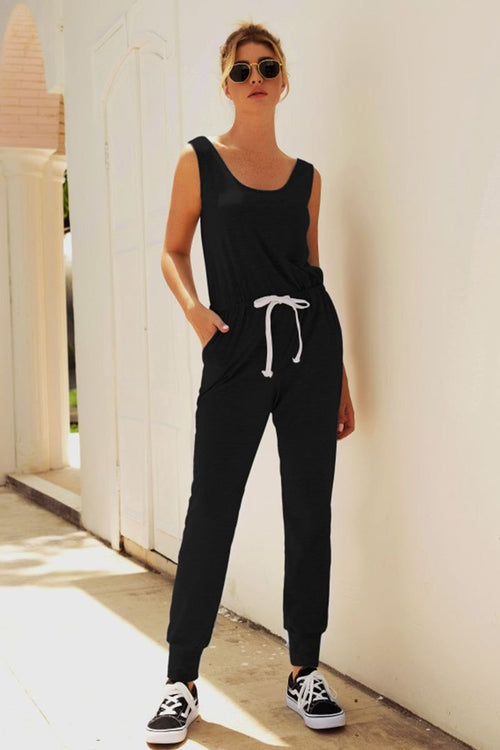 Woman wearing black comfy sleeveless vest pocket jumpsuit with white drawstring and sneakers outdoors