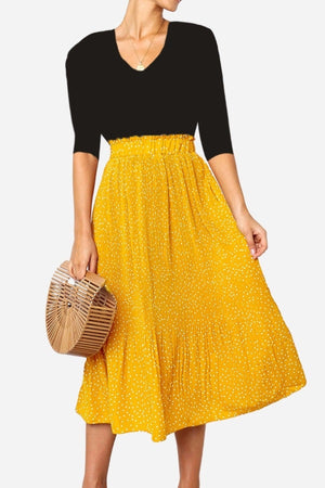 Woman wearing an effortlessly chic yellow polka dot pleated midi skirt with a high waist and black top carrying a wooden handbag.