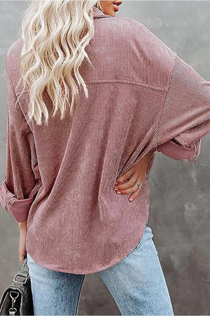 Back view of a woman wearing a sleek suede oversized button-down shirt in dusty rose paired with light blue jeans