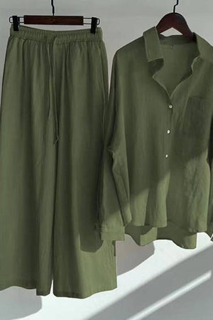 Olive green oversized shirt and palazzo pants two-piece linen set hanging on wooden hangers with natural light shadows