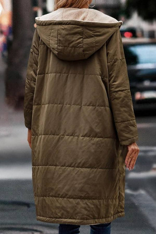 Back view of a woman wearing a long olive green Sherpa-lined hooded teddy coat on a city street.