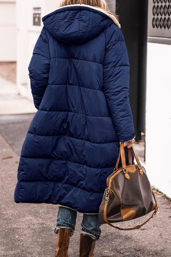 Woman wearing navy Sherpa-lined hooded teddy coat with quilted puffer design and carrying brown handbag outdoors