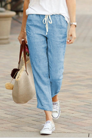 Woman wearing light blue relaxed fit straight pants with drawstring waist and white sneakers walking outdoors carrying a beige tote bag