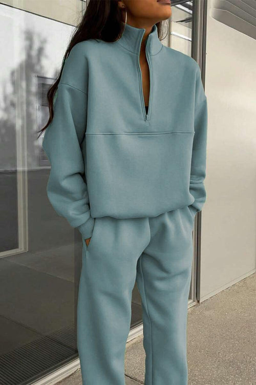 Woman wearing a light blue cotton-blended two-piece tracksuit with high collar and deep zipper standing outdoors.