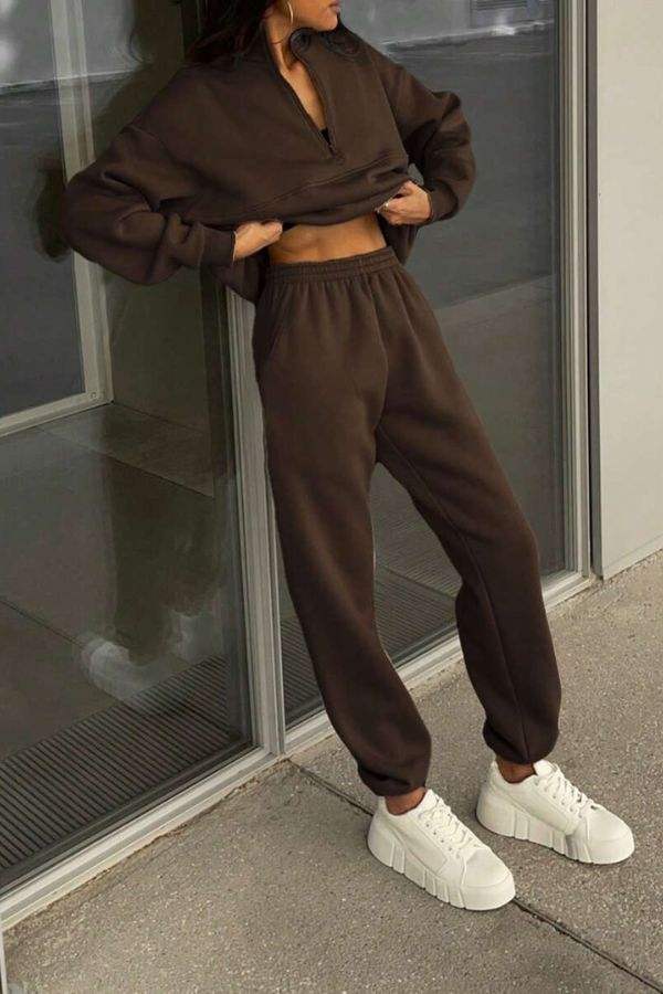 Woman wearing brown cotton-blended two-piece tracksuit with white sneakers standing by glass door