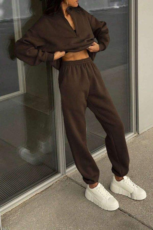 Woman wearing brown cotton-blended two-piece tracksuit with white sneakers standing by glass door