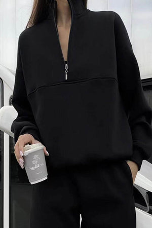 Woman wearing black cotton-blended two-piece tracksuit with high collar and zipper holding coffee cup