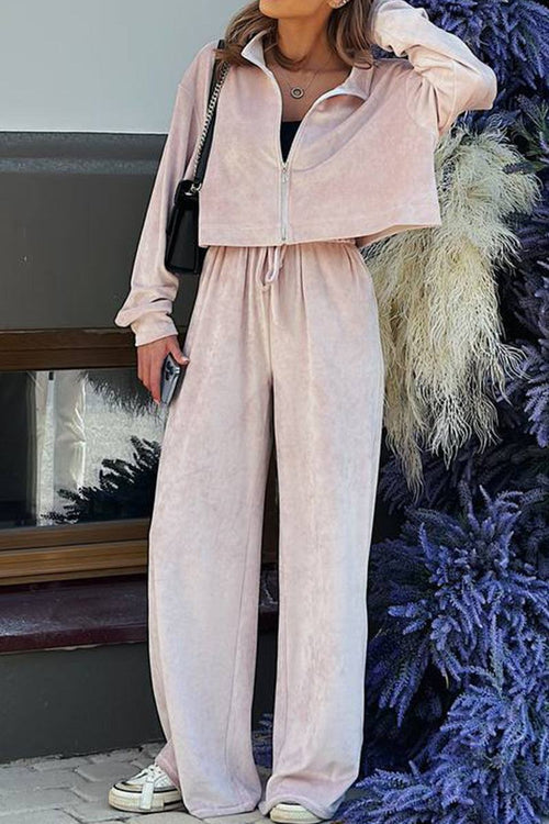 Woman wearing light pink zip up cropped sweatshirt and wide leg pants leisure two-piece co-ord set in velour fabric.