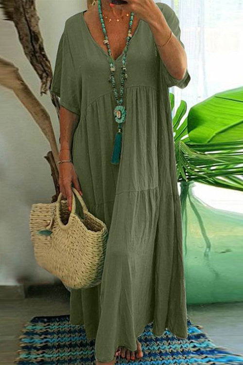 Green V-neck two-tiered maxi swing dress with loose sleeves and flowy silhouette worn with a long beaded necklace and woven handbag