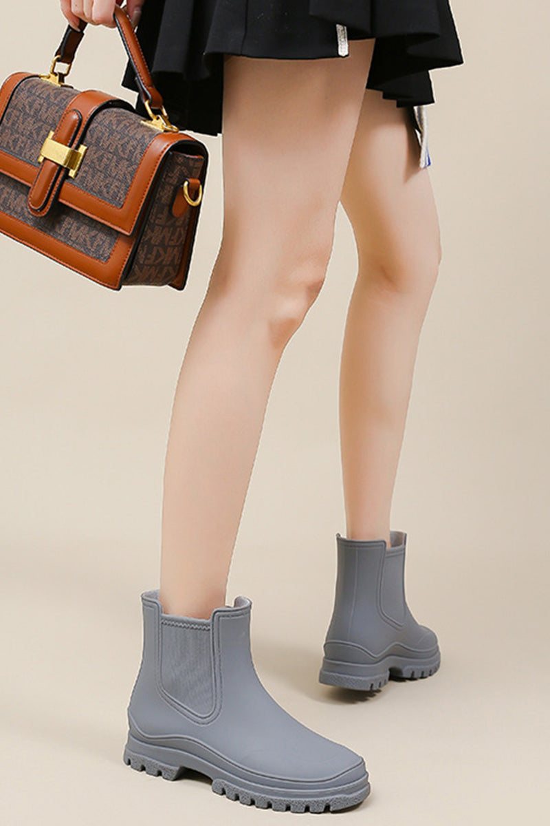 Gray non-slip rain boots with SuperGrip soles worn by person holding brown handbag.