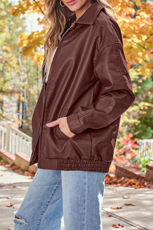 Oversized faux leather motorcycle jacket in brown with relaxed fit and elastic hem, styled with jeans in autumn setting