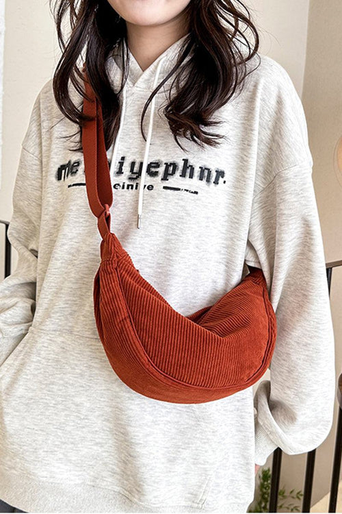 Rust-colored corduroy shoulder bag with adjustable strap worn crossbody with casual hoodie.
