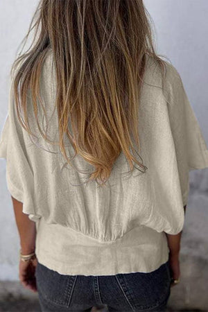 Back view of a woman wearing a beige 100% pure linen short-sleeve blouse with a relaxed fit and natural wrinkles.