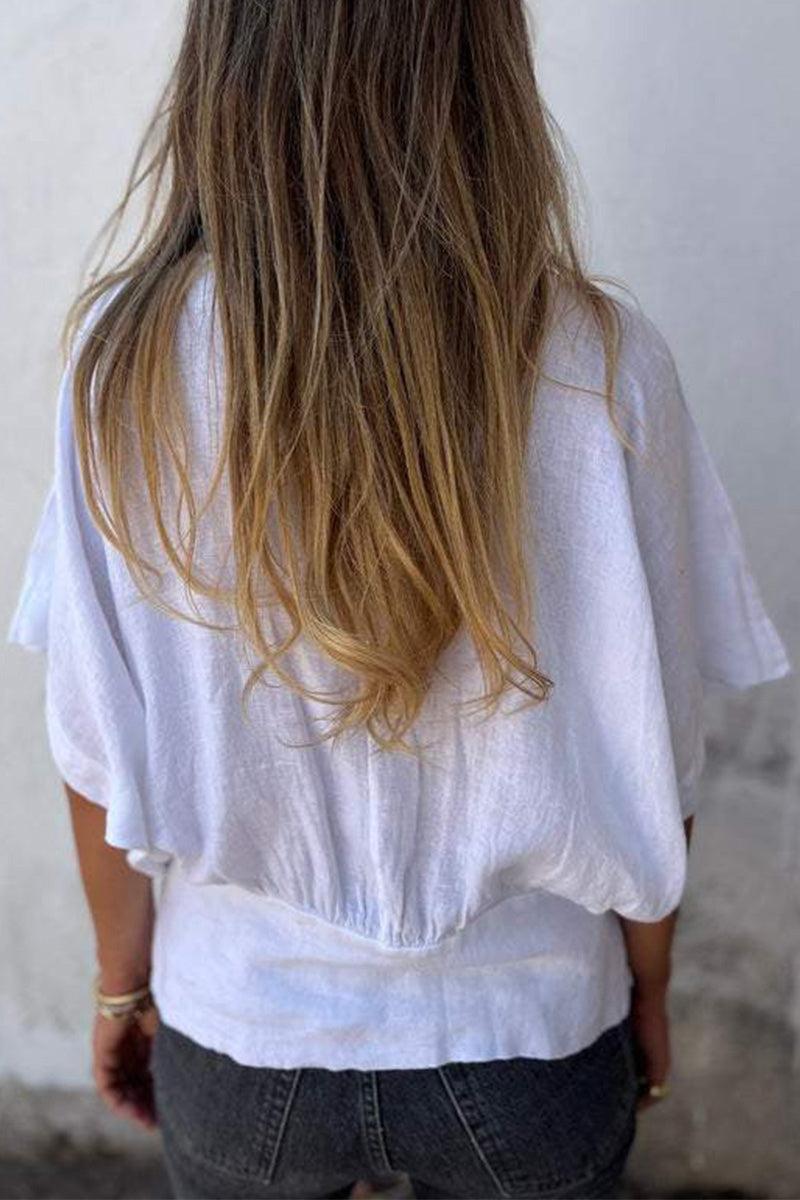 Back view of woman wearing white pure linen short-sleeve blouse with relaxed fit and natural wrinkles, paired with dark jeans.