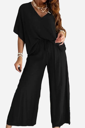 Black two-piece pantsuit with V-neck top and wide-leg pants styled with layered necklaces and bracelets