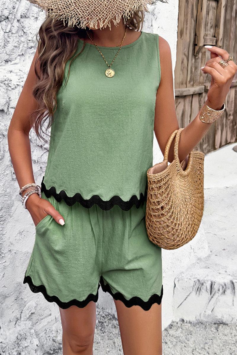 Woman wearing green flattering coastal scallop two-piece set with scalloped black trim, straw hat, and woven bag outdoors