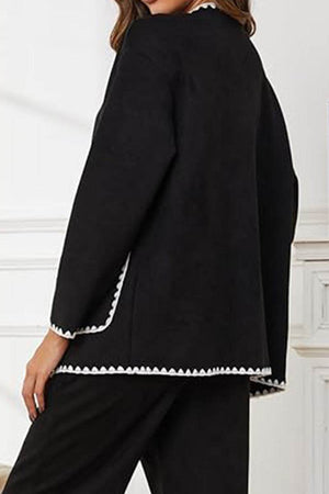 Back view of black contrast-trim knit cardigan with white scalloped edges worn with matching pants.