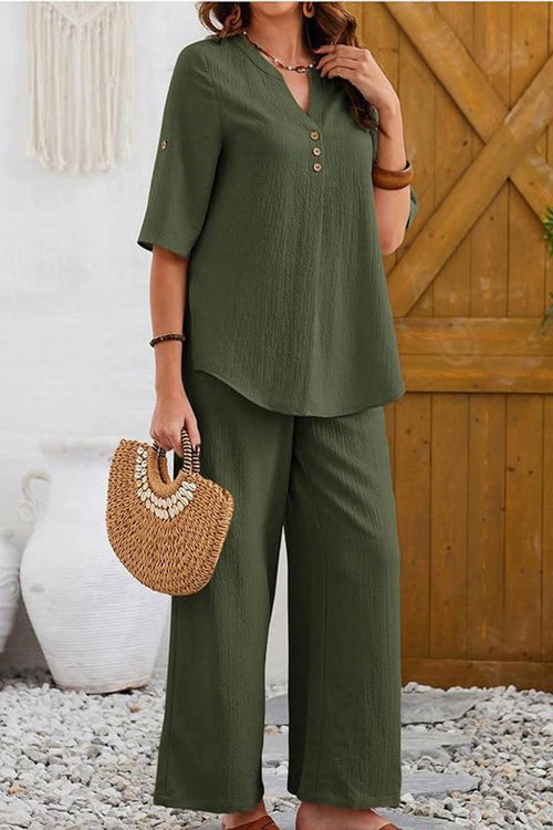 Woman wearing olive green wrinkle-free wide leg pants and matching top set with button details and holding a woven handbag