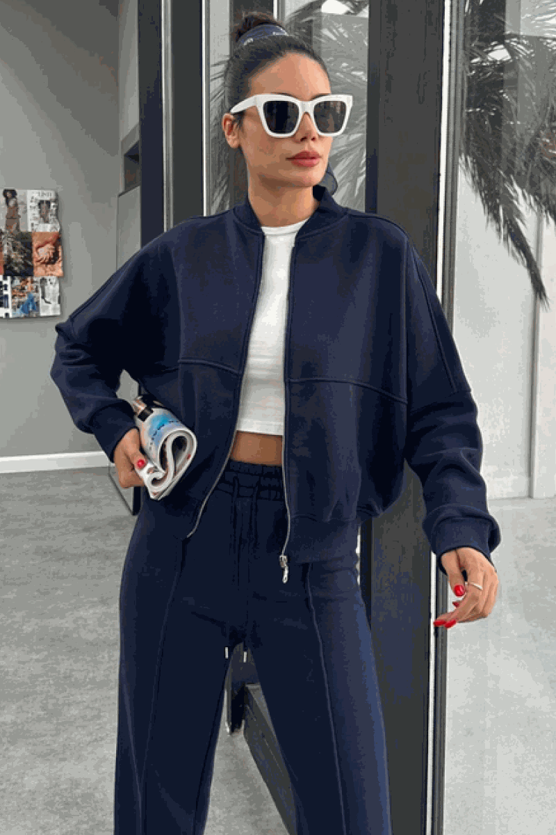 Woman wearing The Voyager Zip Set navy blue zip-front sweatshirt and wide-leg joggers, styled with white crop top and sunglasses