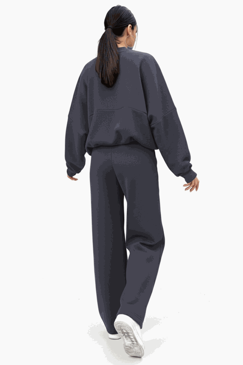 Woman wearing The Voyager Zip Set in dark charcoal, featuring a relaxed zip-front sweatshirt and wide-leg joggers with pockets, styled for comfort and travel.