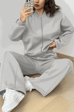 Woman wearing The Voyager Zip Set, light gray zip-front sweatshirt and wide-leg joggers with white sneakers, casual travel outfit