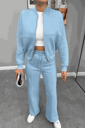 Woman wearing The Voyager Zip Set in light blue, featuring a zip-front sweatshirt and wide-leg joggers with pockets, styled with white sneakers and a white cropped top.