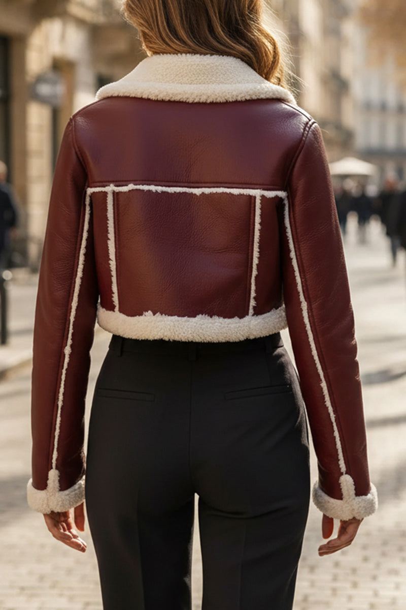 Back view of cropped faux leather sherpa jacket in burgundy with cream sherpa trim worn with black pants outdoors