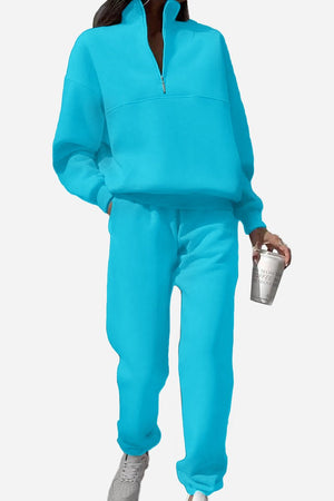 Woman wearing bright blue Classic Airplane Set tracksuit with half-zip pullover and jogger pants holding a coffee cup.