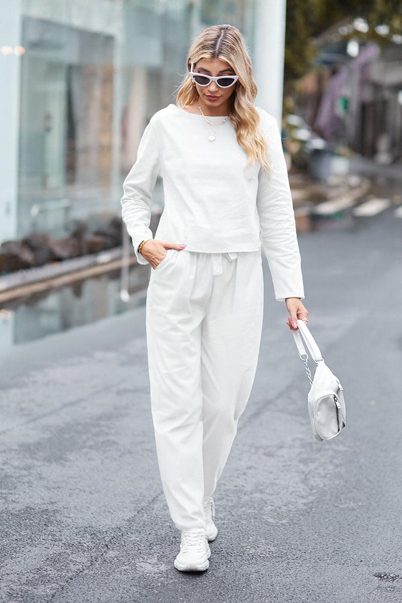 Woman wearing cotton-linen monochrome relaxed longline top and wide-leg pants set walking outdoors with sunglasses and white handbag