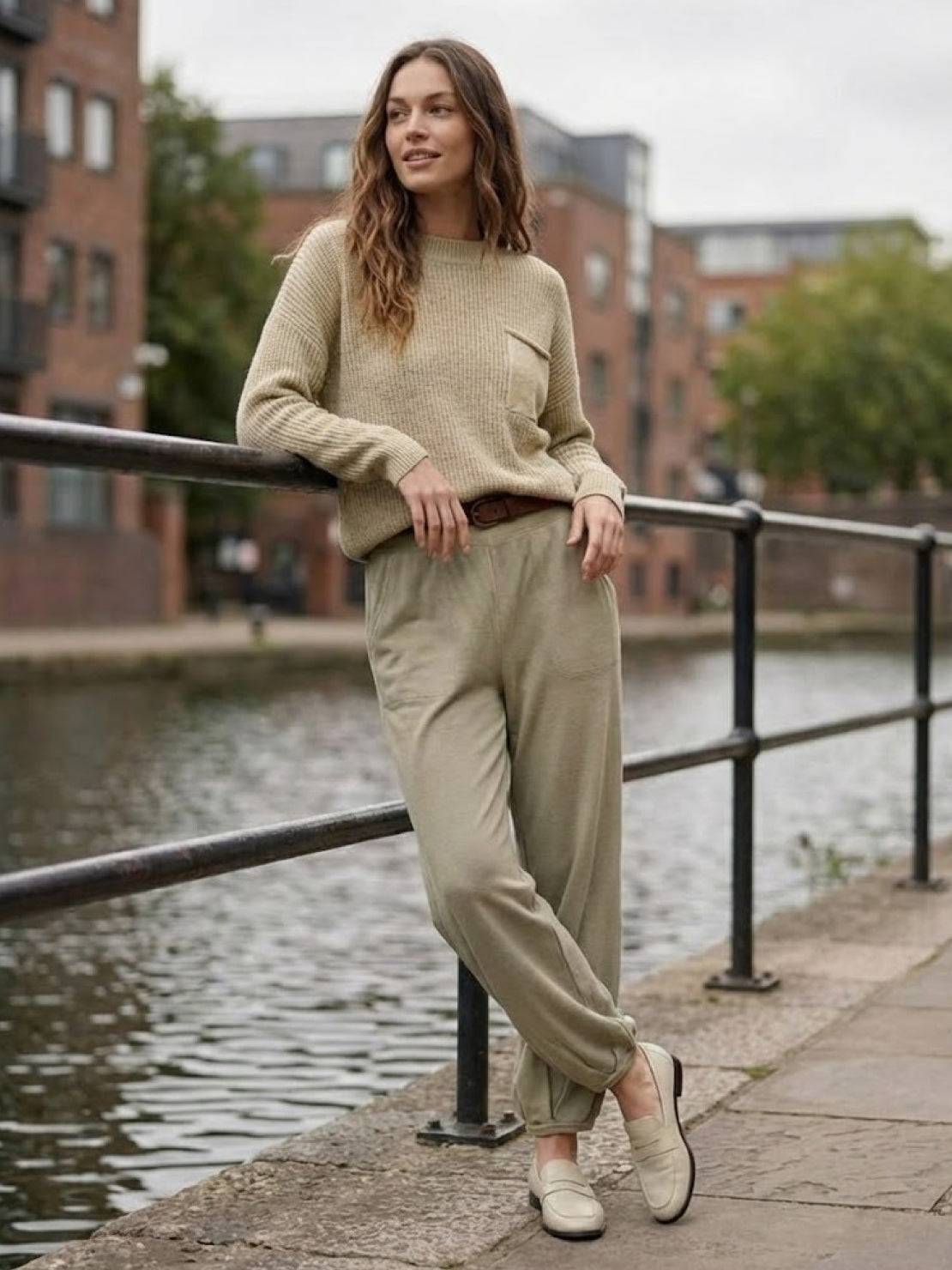 Woman wearing European Minimalism relaxed sweater top and trouser set in neutral khaki by a canal walkway
