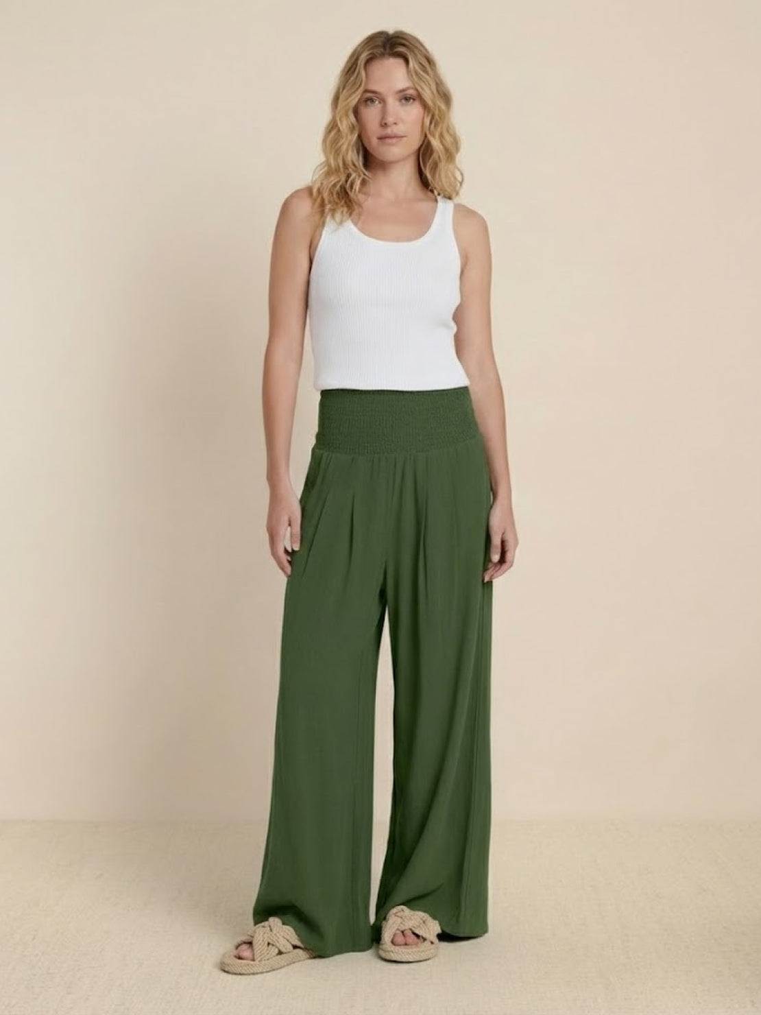 Woman wearing green high-waist cotton linen palazzo pants with white tank top and sandals.