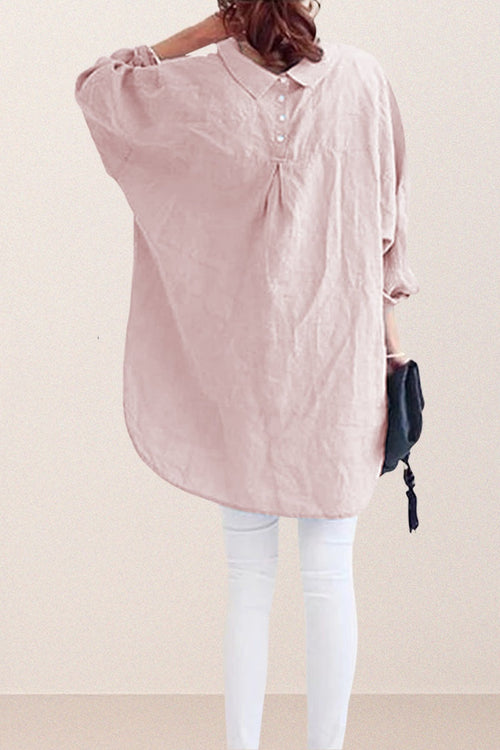 Back view of a woman wearing a pink oversized linen shirt with gathered back yoke and buttons, paired with white pants and holding a black clutch.