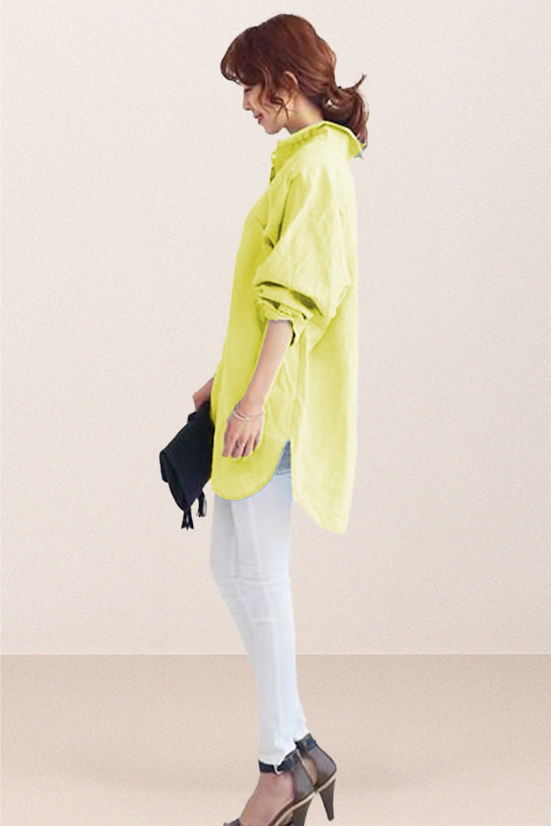 Woman wearing a bright oversized linen shirt with rolled sleeves, white pants, and heels, holding a clutch bag.