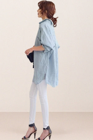 Woman wearing oversized light blue linen shirt with rolled-up sleeves and white pants