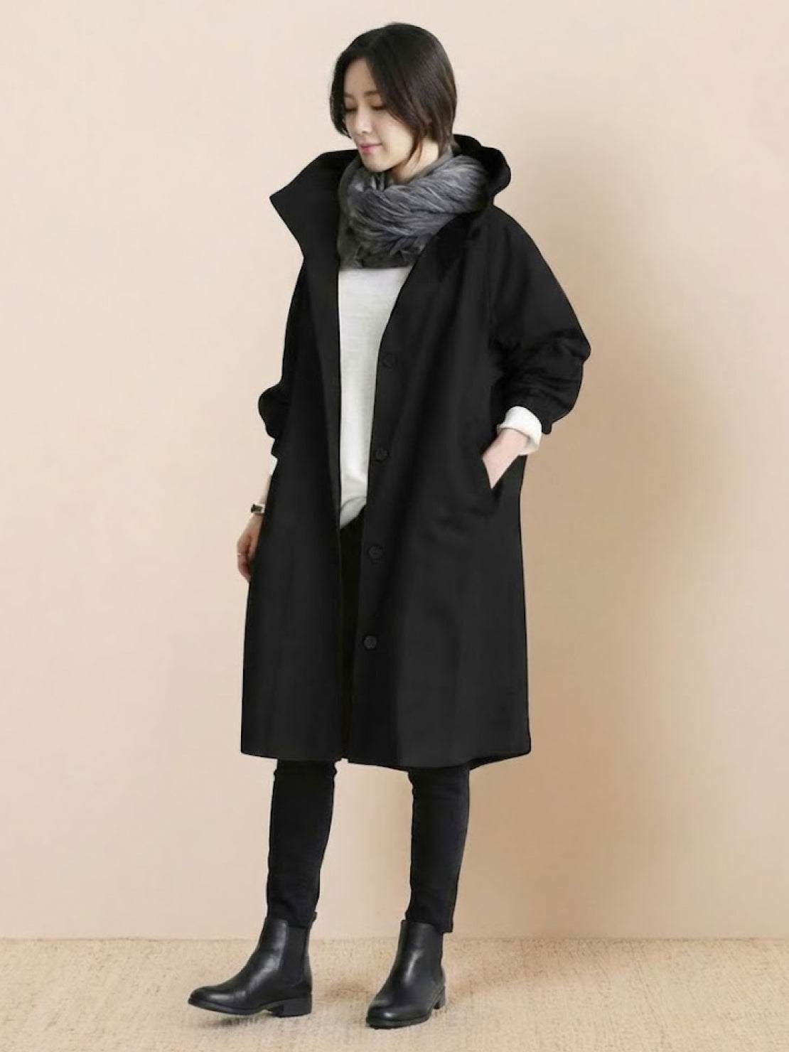 Woman wearing black oversized Rain Couture Windbreaker with scarf and boots against beige background