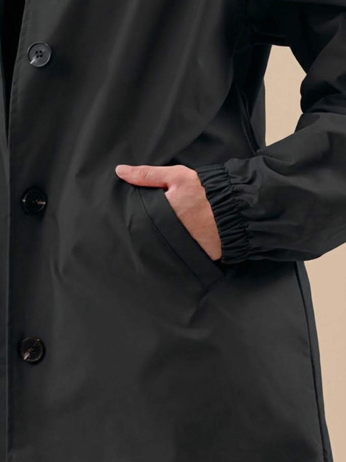Close-up of black Rain Couture Windbreaker jacket showing water-resistant fabric, button closure, and elastic cuff sleeve on model's arm.