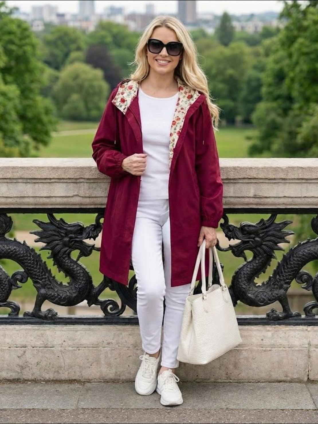 Woman wearing burgundy Rain Couture Windbreaker with floral hood lining, white outfit, sunglasses, and white handbag outdoors