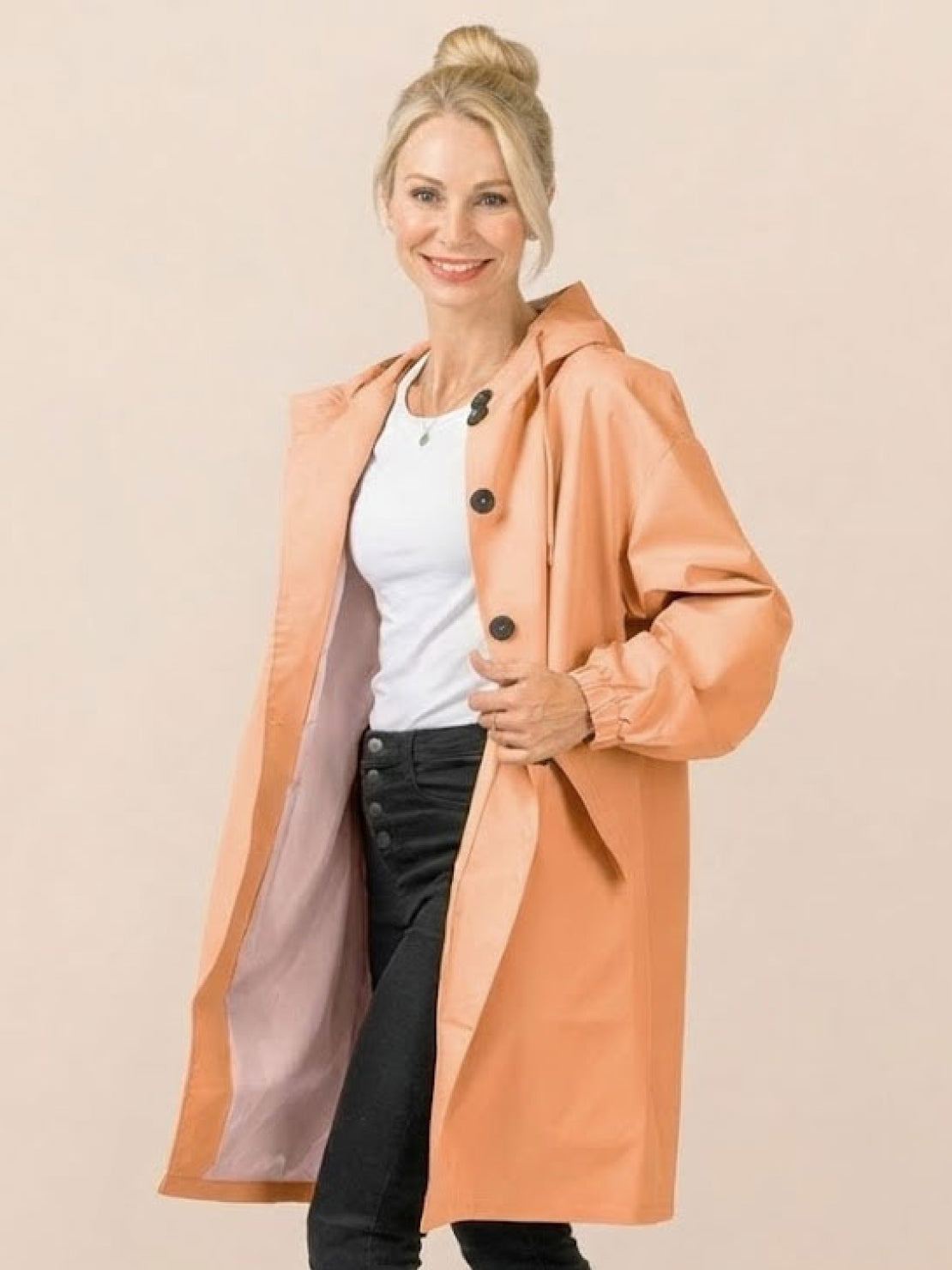 Woman wearing trendy oversized peach Rain Couture Windbreaker with hood and black buttons over white top and black pants
