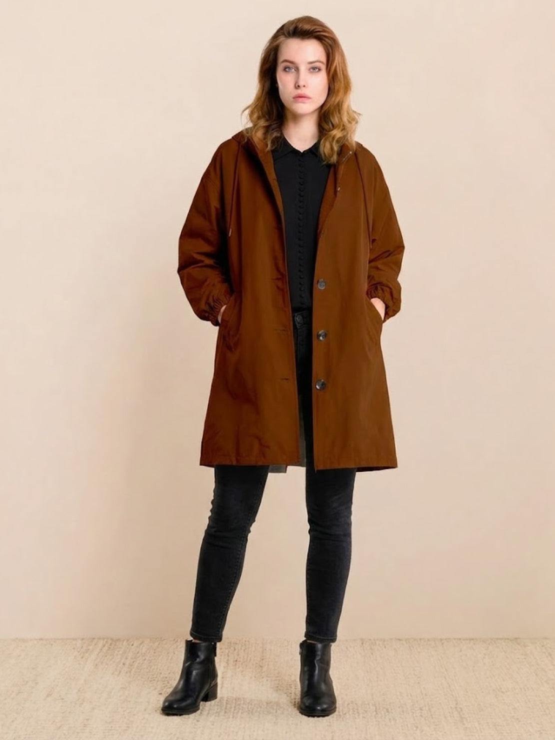 Woman wearing brown oversized Rain Couture Windbreaker with black outfit and boots against beige background