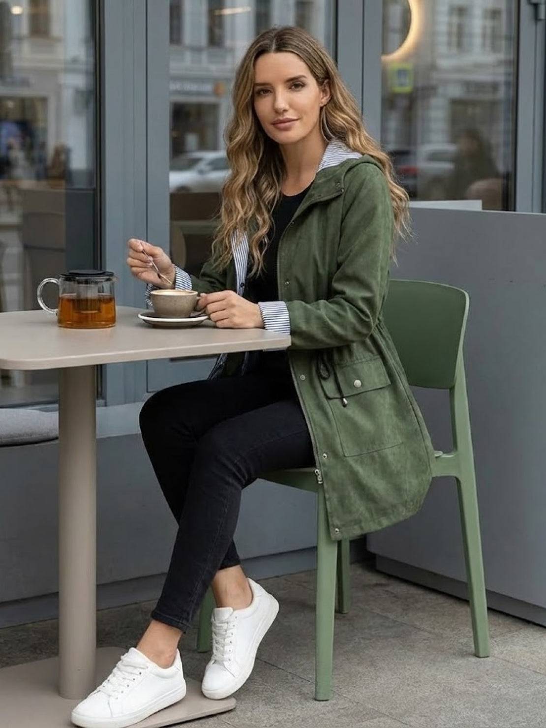 woman wearing green water resistant windbreaker sitting at cafe table drinking coffee