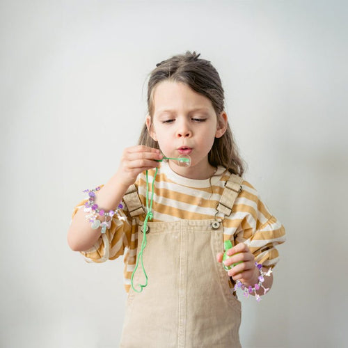 Child wearing bracelets and blowing bubbles, showcasing creativity with bracelet-making kit for kids.