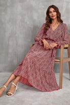 Woman wearing Bloom Wrap Midi Dress with floral print and trumpet sleeves sitting on wooden chair against gray background