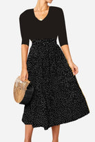 Woman wearing an effortlessly chic polka dot pleated high-waist midi skirt set with pockets and a black top holding a wooden handbag