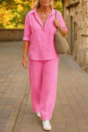 Woman wearing a pink relaxed shirt and trousers two-piece set with white sneakers and a woven bag outdoors