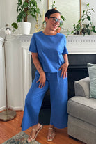 Woman wearing a blue loose fit co-ord set with short sleeves and wide-leg trousers in a cozy living room.