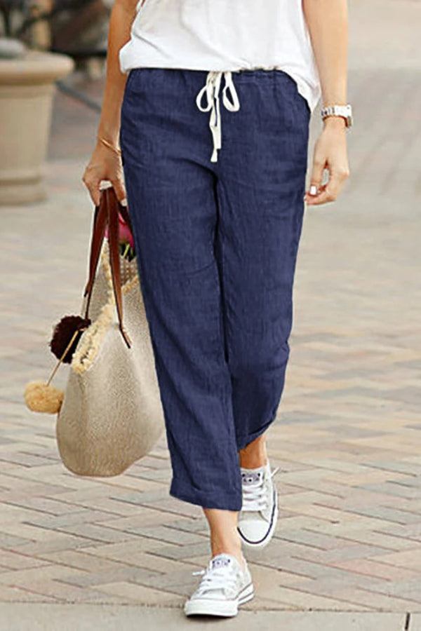 Woman wearing navy relaxed fit straight pants with white drawstring and casual white sneakers walking outdoors carrying a beige tote bag