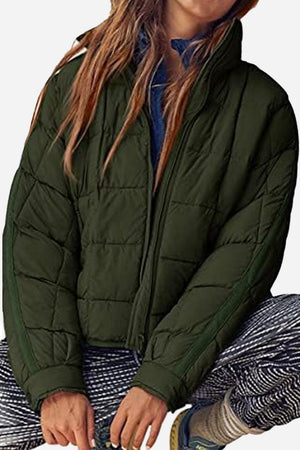 Woman wearing dark green lightweight puffer travel jacket with full front zipper and casual pants sitting relaxed