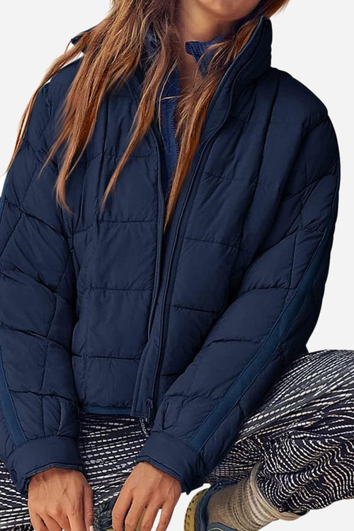 Lightweight navy blue puffer travel jacket worn with patterned pants, featuring quilted design and front zipper closure