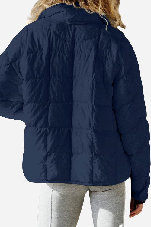 Back view of navy blue lightweight puffer travel jacket worn by person with blonde hair and gray leggings