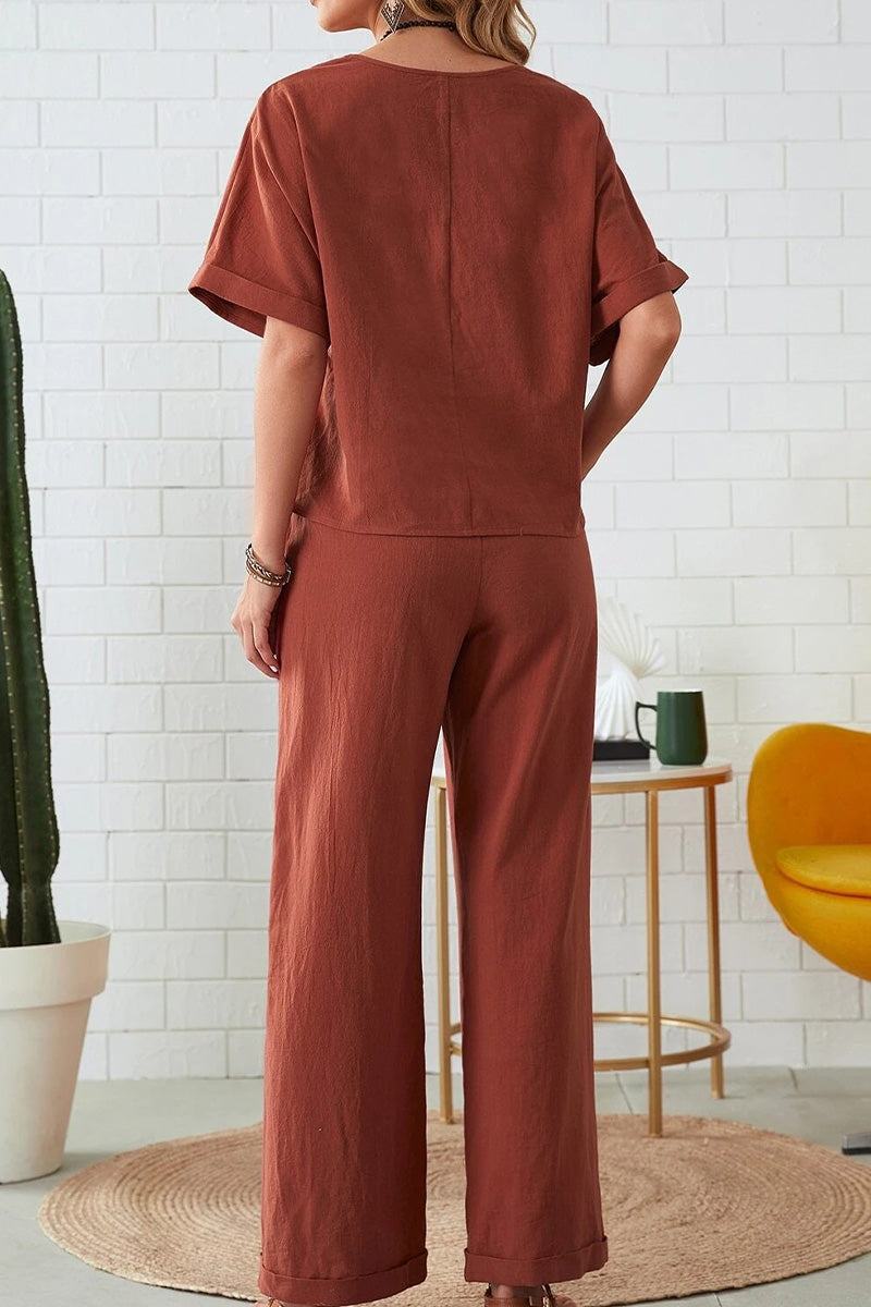 Woman wearing brown rolled cuff top and patch pocket pants set standing indoors with plants and furniture in background